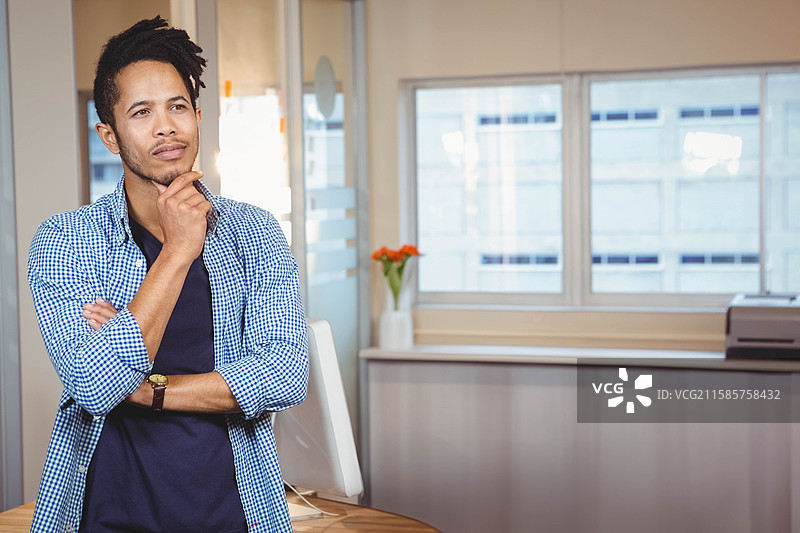 非裔美国男性在办公室的桌子前凝视，桌上有显示器和花瓶，留白空间图片素材