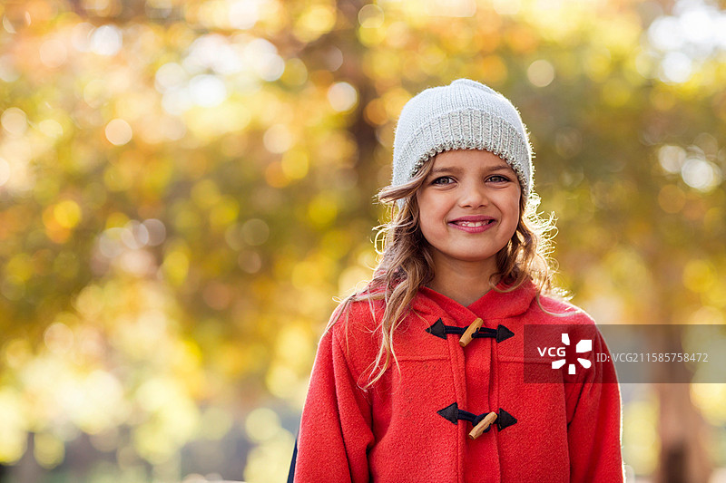 孩子在秋天的公园里穿着红色扣子外套和浅灰色针织帽子。图片素材