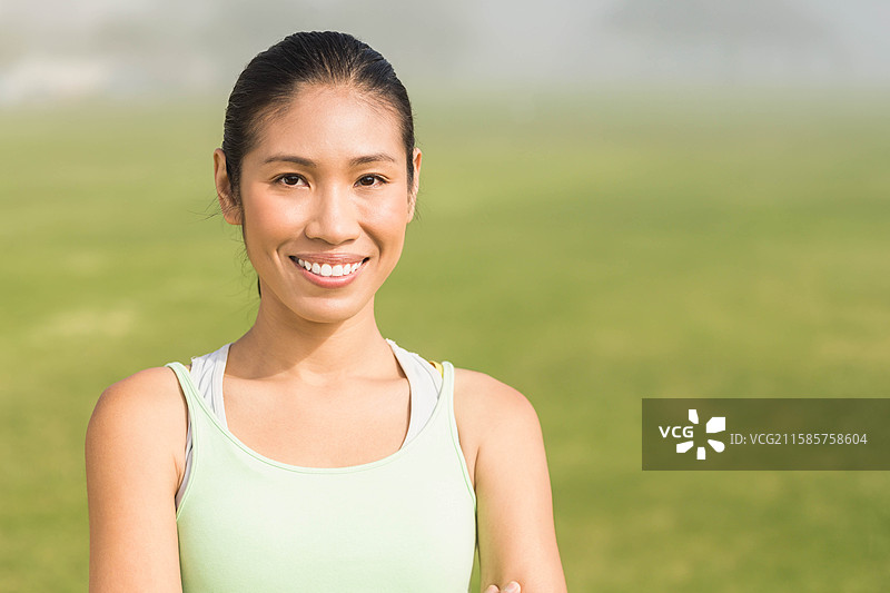 一位成年女性双臂交叉，站在开阔的草地公园里，阳光明媚的天空下。图片素材