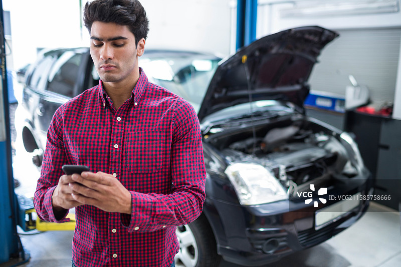 亚洲男子在修理车库检查智能手机，旁边有掀背车升降工具柜，留白空间图片素材