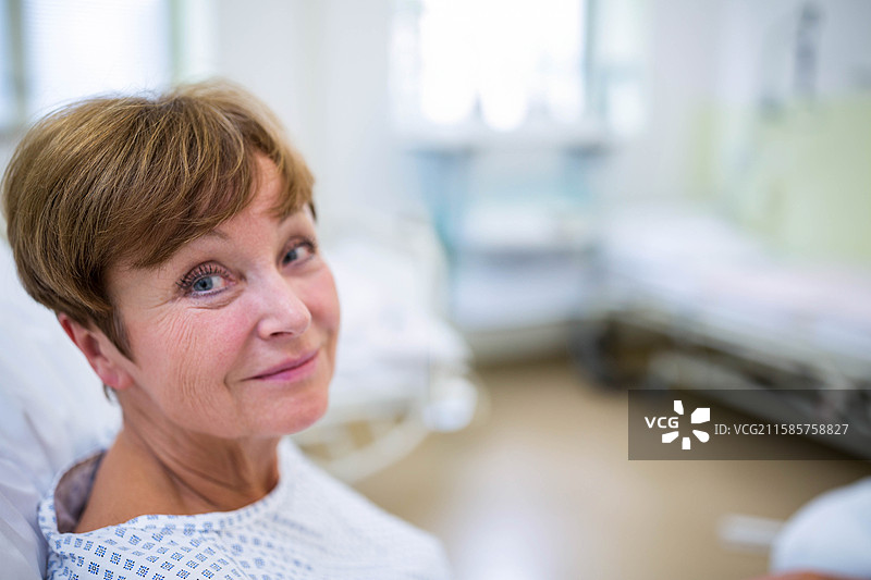 一位穿着图案病服的老年女性在病房的医院床上靠着，旁边是空床。图片素材