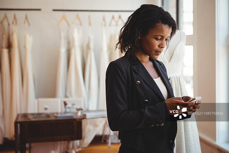 非裔美国女性在婚纱店的桌子旁查看智能手机，旁边有模特和婚纱，留白空间图片素材