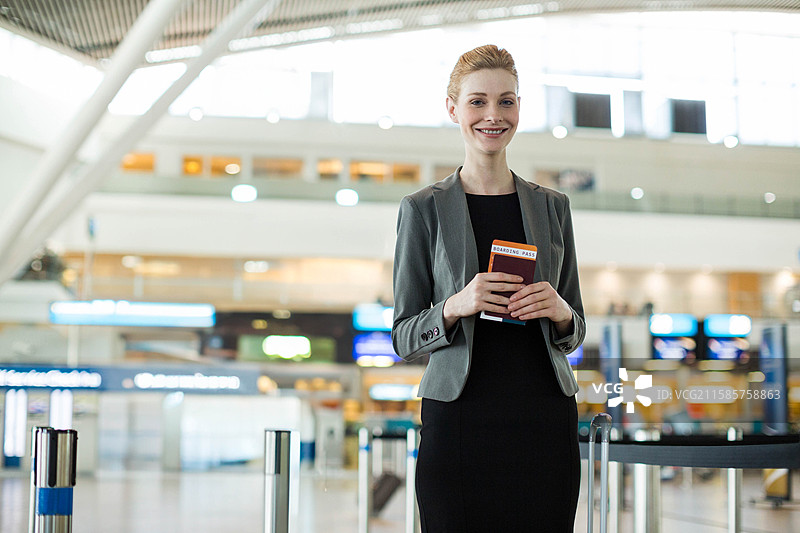 护照和登机牌放在机场航站楼的安全带隔离栏上，旁边是发光的自助值机 kiosks。图片素材