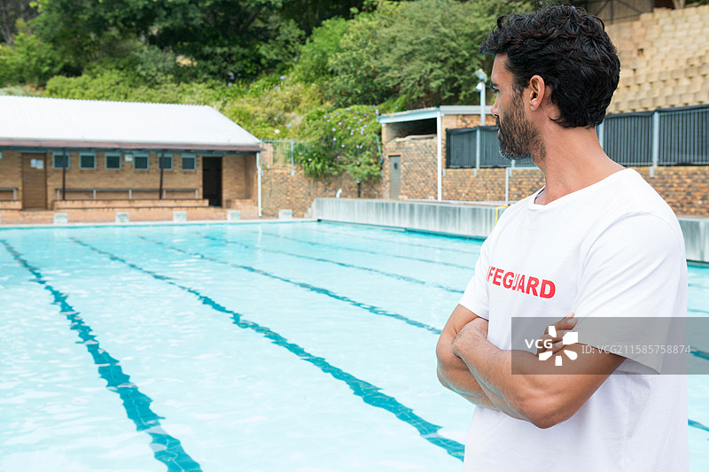 救生员在游泳池边值班，旁边有泳道标记和砖砌更衣室。图片素材