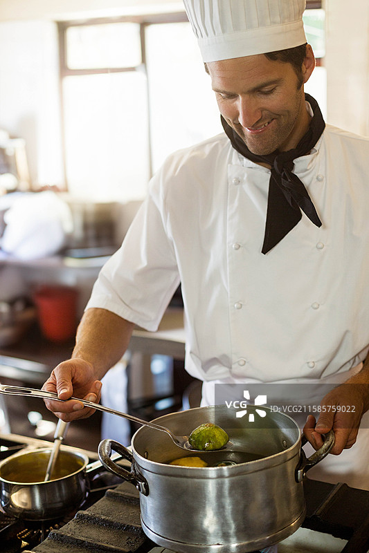 男厨师穿着制服，在餐厅厨房的煤气炉上搅拌钢锅中的绿色蔬菜图片素材