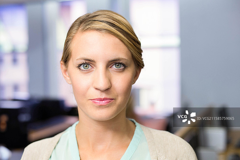 穿着开衫和衬衫的职业女性站在开放式办公室，周围有桌子和窗户。图片素材