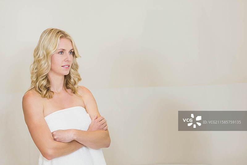 穿着白色毛巾的女性站在中性色调的水疗更衣室墙壁前，留有空白空间图片素材