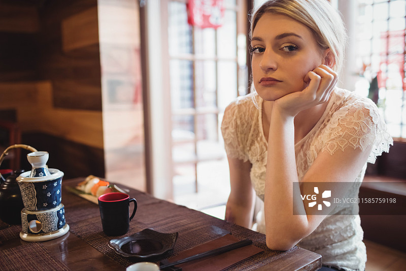 女子在日本餐厅的桌子上用手托着头，旁边有陶瓷茶壶和寿司。图片素材