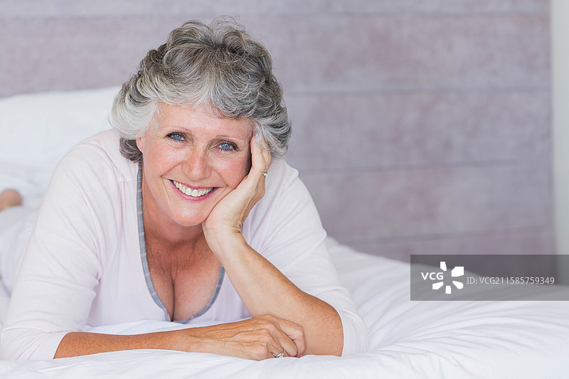 穿着粉色睡衣的老年女性趴在床上，手上戴着戒指，背景是木质墙壁。图片素材