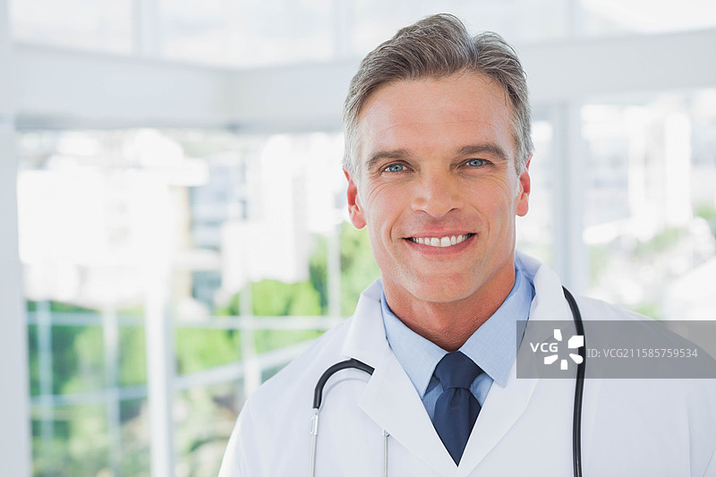 穿着白大褂和听诊器的男性医生站在诊所的玻璃窗旁，留有空白空间图片素材