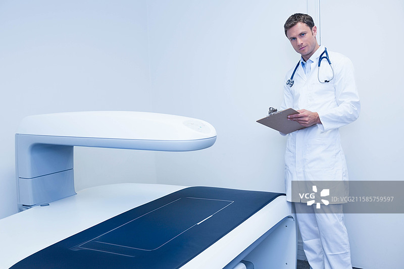 医疗成像扫描仪静置在临床检查室内，旁边有一个夹板。图片素材