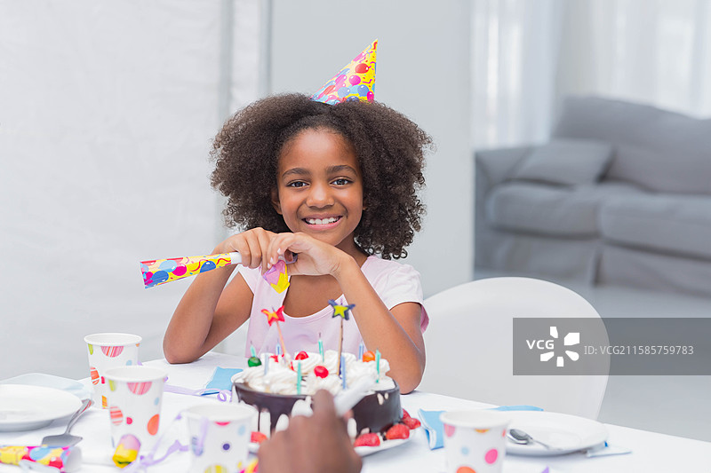 非裔美国小孩微笑着，戴着派对帽，坐在家里的餐桌旁，面前有巧克力蛋糕。图片素材