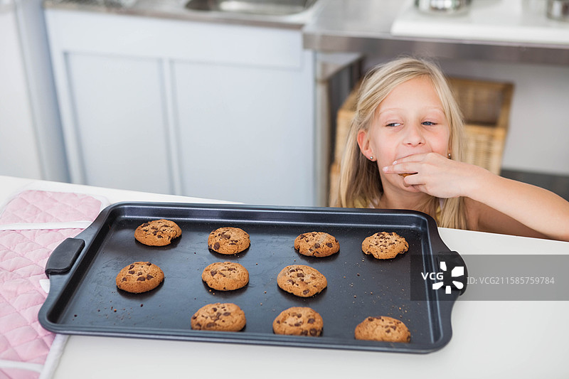 金发女童站在厨房台面前，伸手去拿托盘上的饼干，留白空间图片素材
