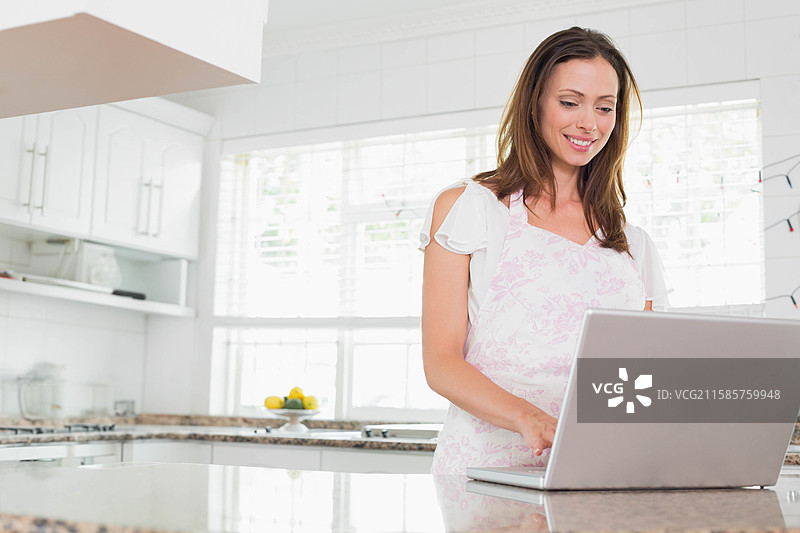 中年女性在大理石厨房岛上使用银色笔记本电脑，旁边放着一碗柠檬。图片素材