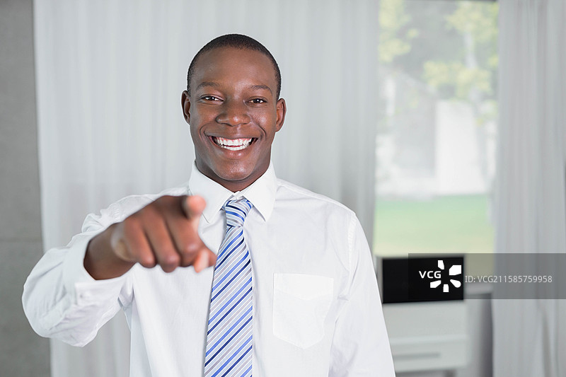 一位非裔美国男性在明亮的家庭办公室中指向观众，身后有一台黑色显示器。图片素材