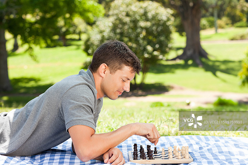 男子在公共公园的野餐毯上用木制棋盘下棋，留有空白空间图片素材