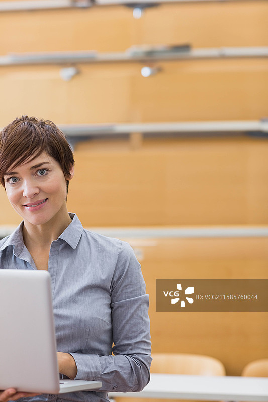 在讲堂的桌子上，女人正在使用笔记本电脑，周围有木制长椅和栏杆，留有空白空间。图片素材