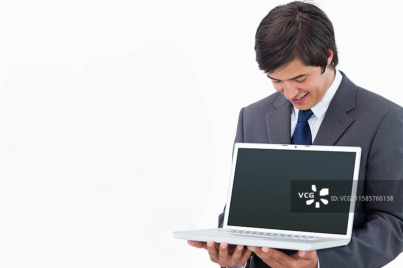 身穿西装的商人在工作室里微笑着看着手中空白屏幕的笔记本电脑，留有空白空间。图片素材