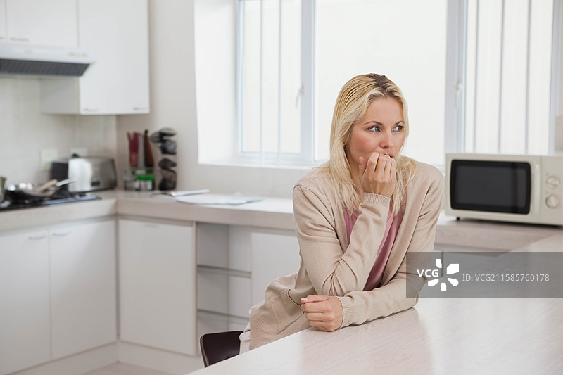 穿着休闲服的女性靠在白色厨房岛上咬指甲，旁边有文件，留有空白空间图片素材