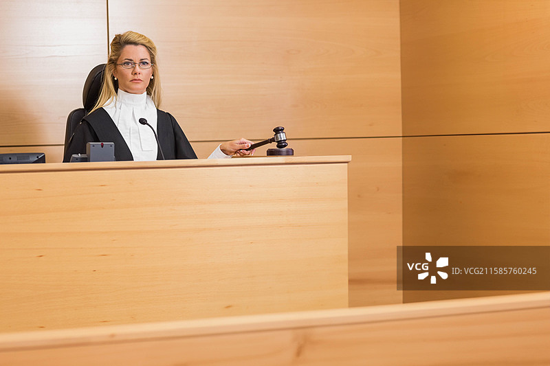 穿着法袍的女性法官在法官席上手持木槌，旁边有麦克风和设备，留有空白空间图片素材