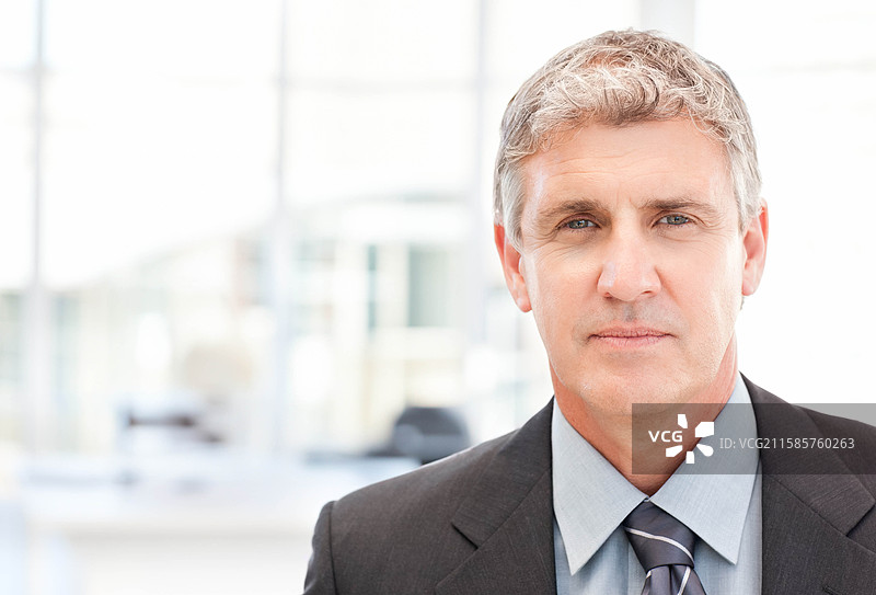 中年男性穿着西装和领带站在现代办公室，靠近桌子和显示器，留有空白空间图片素材