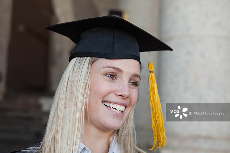 女性微笑着庆祝毕业，戴着学位帽，站在拱形入口下。图片素材