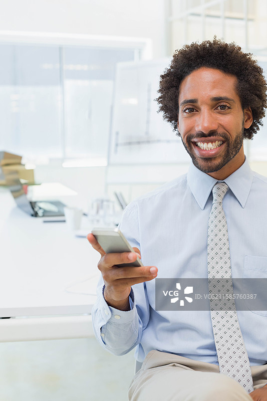 非裔美国男性坐在办公室的桌子旁，手持智能手机，白板背景，留有空白空间图片素材