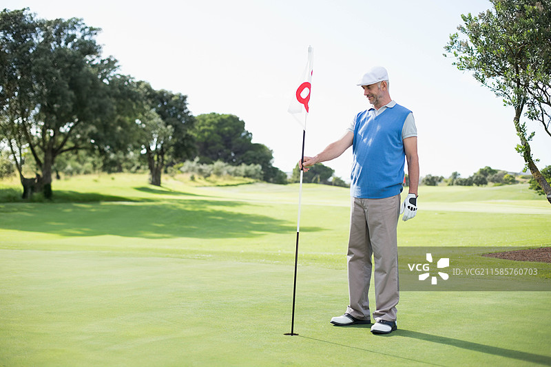 穿着高尔夫手套的男性高尔夫球手站在果岭上，手握旗杆，旁边有空白空间。图片素材