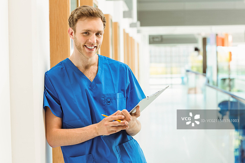 医疗专业人员靠在医院走廊的柱子上，手里拿着夹板和铅笔。图片素材