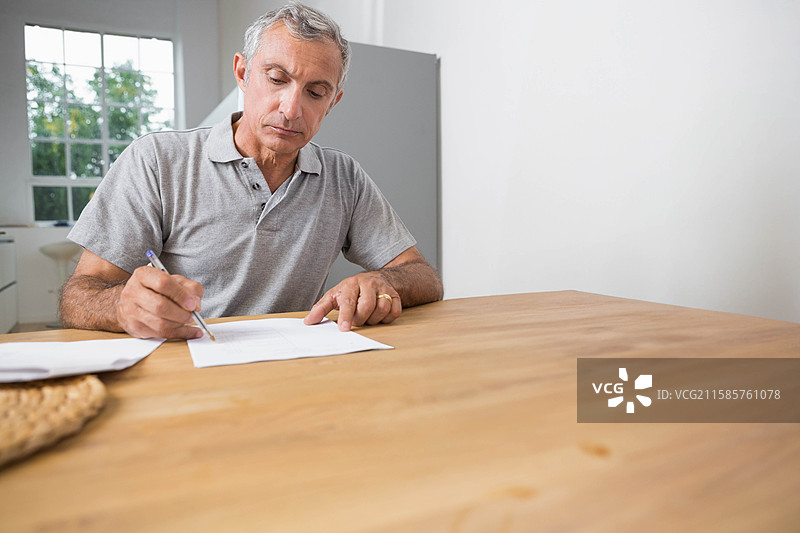 在家办公的木桌上，男人正在签署文件，旁边有一个编织篮和一支钢笔，留有空白空间。图片素材