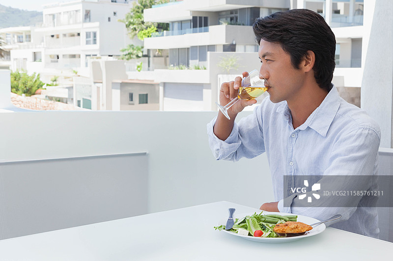 中年日本男子在阳台上品尝白葡萄酒，享用沙拉，旁边有胡椒磨，留有空白空间图片素材