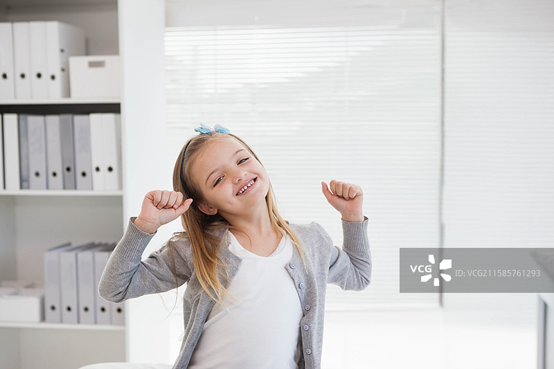 白人女孩在家中的办公桌前伸展双臂，桌上有文件夹、盒子和百叶窗。图片素材