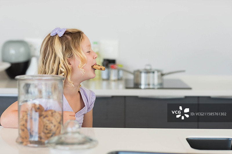 小女孩伸手去拿白色厨房台面上的巧克力饼干玻璃罐，留白空间图片素材