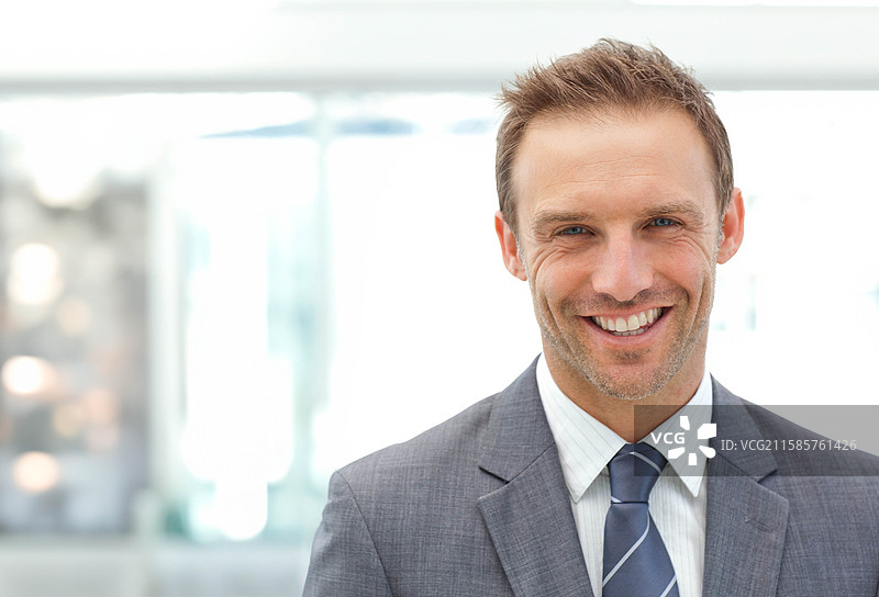 穿着灰色西装和蓝色条纹领带的商务高管站在大堂的玻璃隔断旁。图片素材
