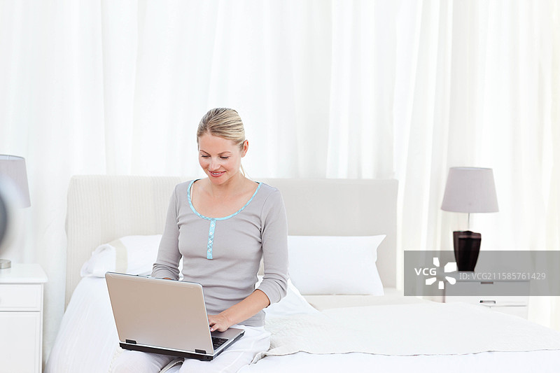 笔记本电脑放在整洁的床上，床单洁白，明亮的极简风格卧室。图片素材