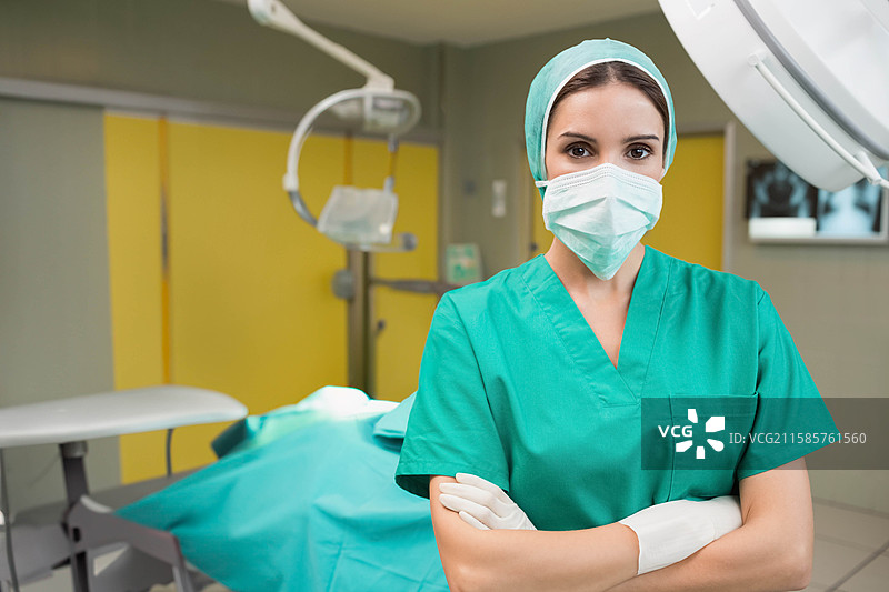 女性外科医生在手术室中交叉双臂，背景有手术台、手术灯和X光显示器，留有空白空间。图片素材