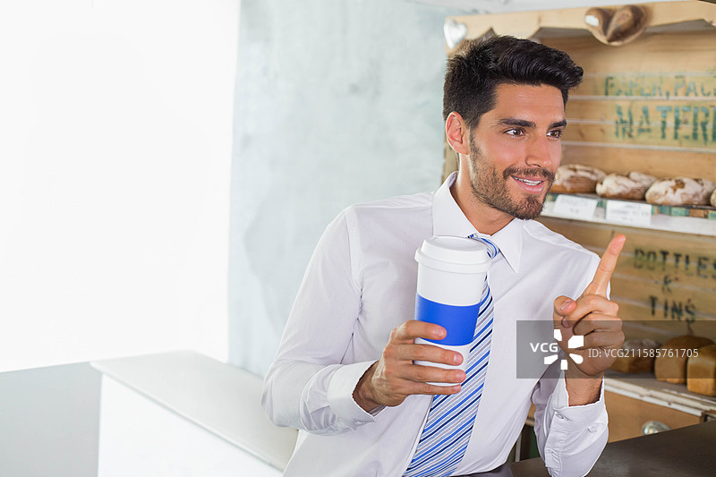 穿着衬衫和领带的成年男子靠在咖啡馆柜台上，手持外带杯，抬起手指，留有空白空间。图片素材