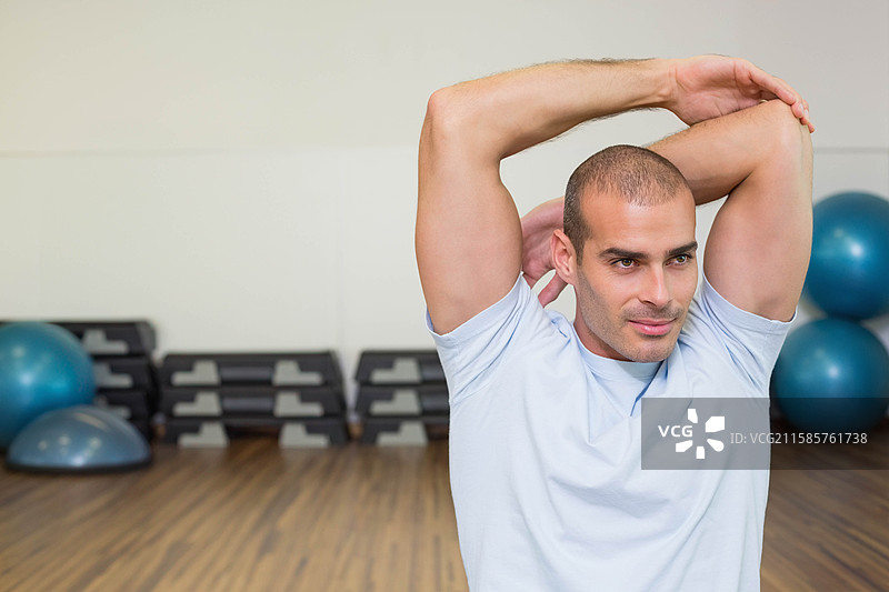 男子在健身房工作室中进行三头肌拉伸，周围有稳定球和踏板，留有空白空间图片素材
