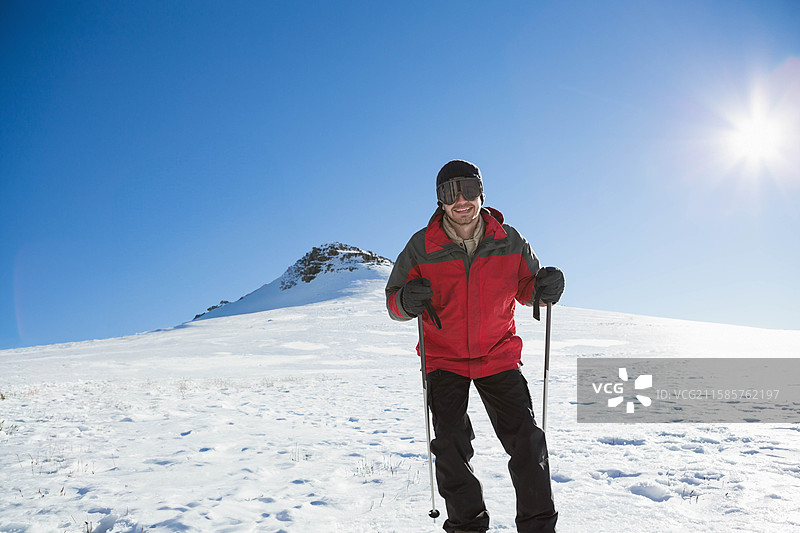 滑雪者在蓝天和阳光下，手持滑雪杖在雪坡上滑行，留有空白空间。图片素材