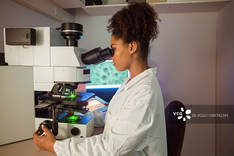 在研究实验室的工作台上，荧光显微镜发出绿色光线照射在载玻片上，旁边有架子。图片素材