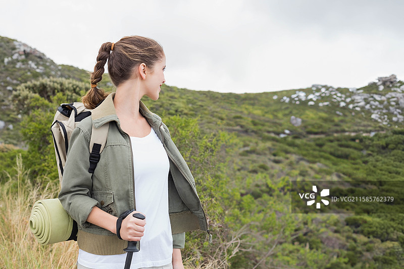 背包 resting 在多云天空下的草地山坡上，周围有散落的岩石和低矮的灌木。图片素材