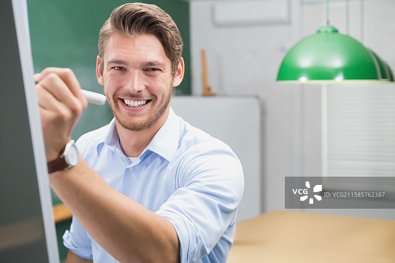 男子在教室桌子上用马克笔在白板上展示想法，绿灯下。图片素材