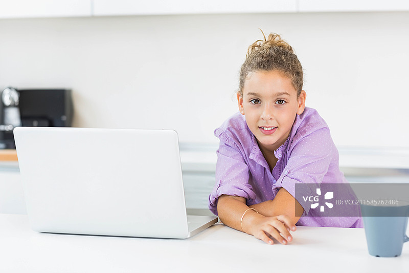 女孩在厨房台面上使用银色笔记本电脑，旁边是黑色咖啡机，留有空白空间。图片素材