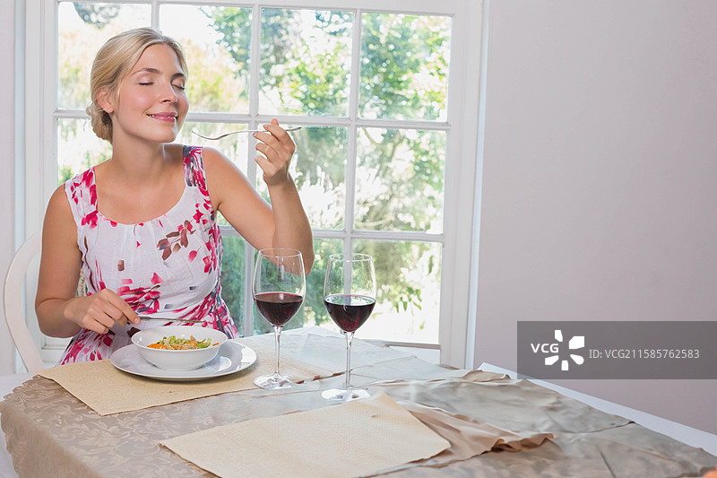 二十多岁的女性在靠窗的餐桌上吃沙拉，旁边有一杯酒，留有空白空间。图片素材
