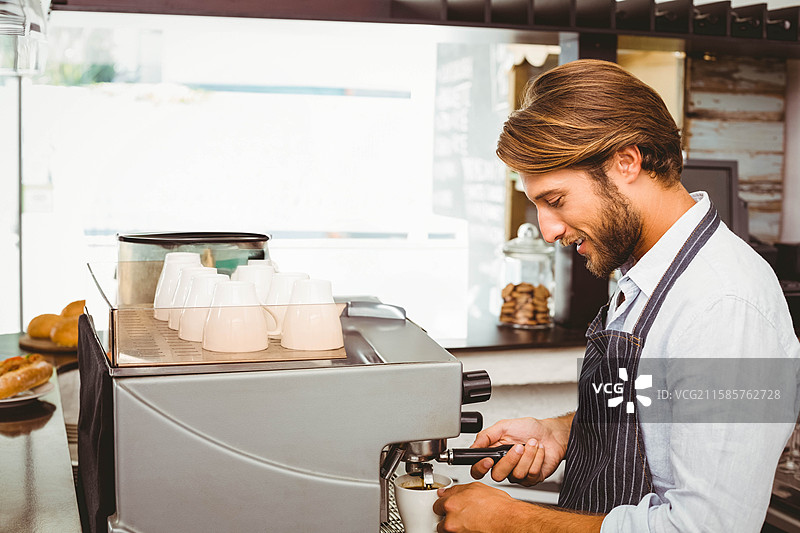 穿着条纹围裙的男咖啡师在咖啡馆操作意式咖啡机，旁边有糕点，留有空白空间图片素材