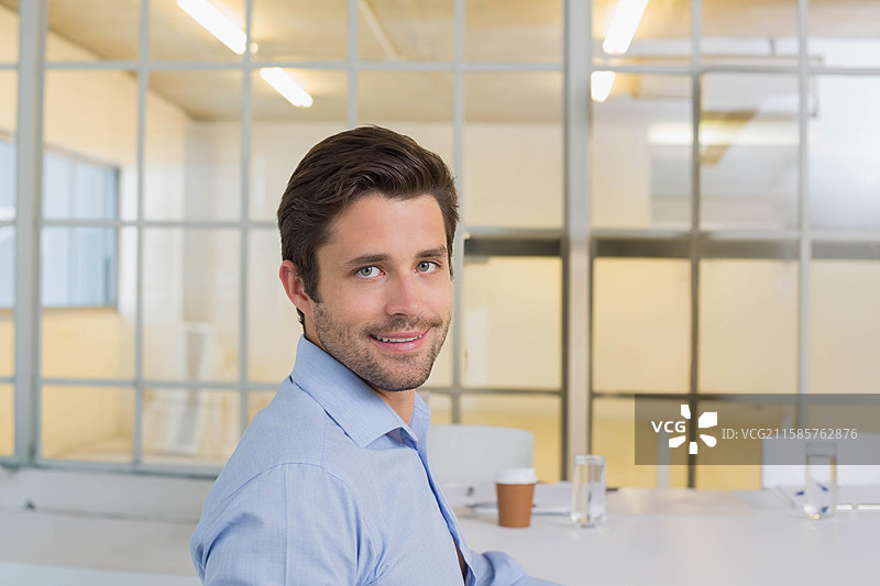 白人男性专业人士坐在会议桌旁，手持纸杯咖啡，旁边是玻璃面板。图片素材