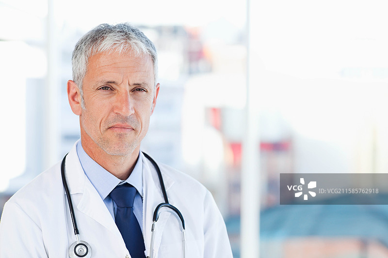 穿着白大褂和听诊器的男性医生站在诊所接待区，留有空白空间图片素材