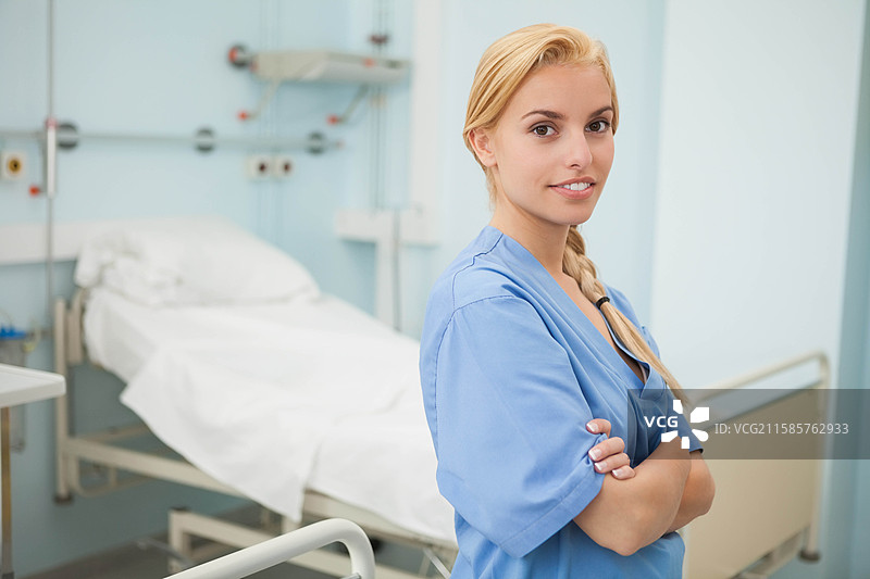 穿着蓝色护士服的女性护士站在病房的床边，旁边有气体出口，留有空白空间图片素材