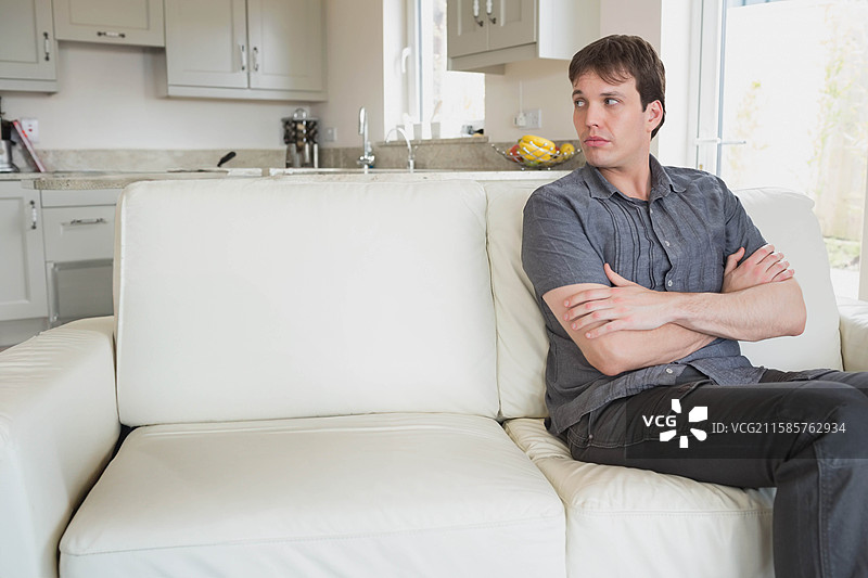 男人坐在厨房的白色皮沙发上，旁边是带有水果碗的花岗岩台面，留有空白空间。图片素材