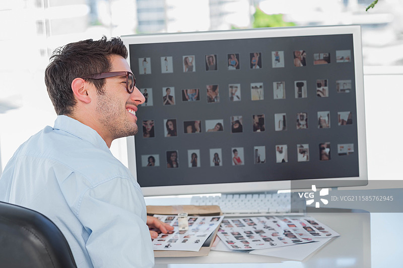 桌子上放着的文件夹，旁边是显示缩略图网格的显示器，阳光透过窗户洒进来。图片素材